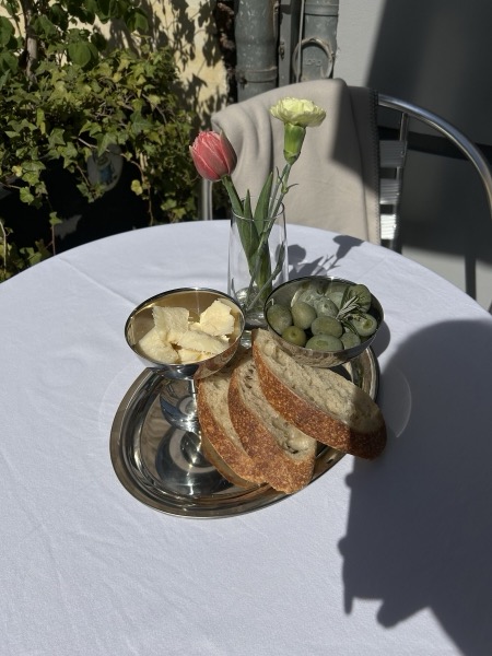 Brot, Oliven und Butter auf einer Silberetagere, daneben Tulpen auf weißem Tuch.