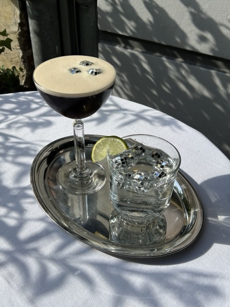 Ein Espresso Martini mit drei Kaffeebohnen auf einem Silbertablett im Blattschatten.