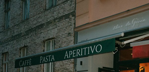 Die grüne Markise der Bar mit der Aufschrift CAFFÈ PASTA APERITIVO, daneben der Schriftzug Bar la Gioia am Fenster, am Abend des Markenevents.