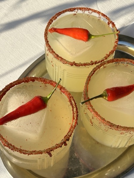 Drei Spicy Margaritas mit Salzrand und roter Chilischote auf einem Silbertablett.
