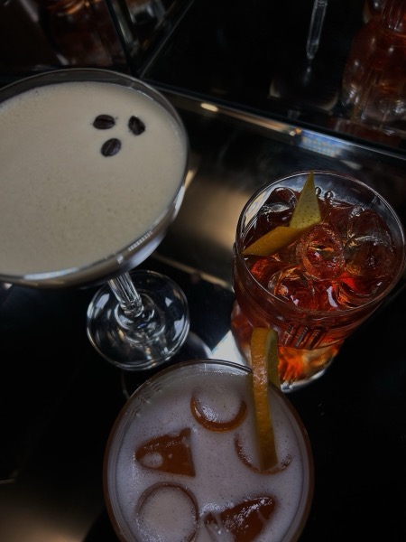 Espresso Martini, Negroni und ein Sour nebeneinander auf dunklem Tresen.