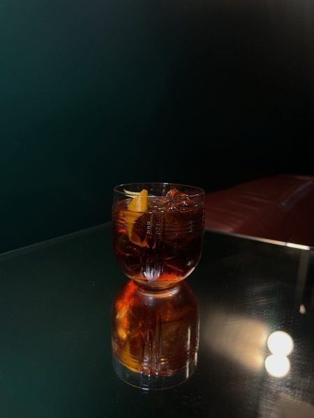 Ein Negroni mit Orangenzeste auf einem dunklen Tisch, im Glas spiegelt sich das Licht.